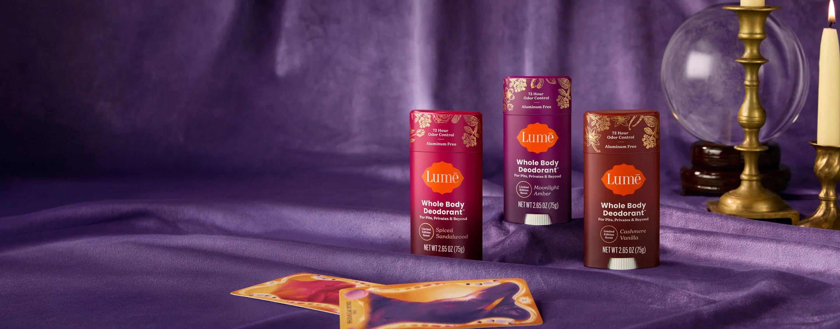 Three Lume deodorants in front of a crystal ball and a luxe purple curtain