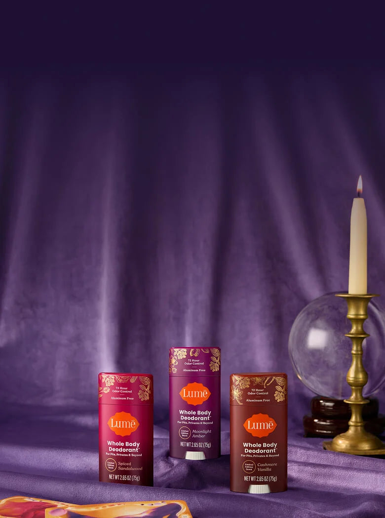Three Lume deodorants in front of a crystal ball and a luxe purple curtain
